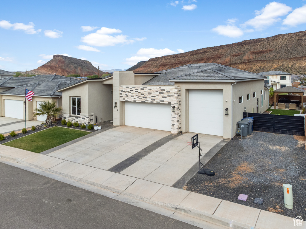 View of front of house with stucco siding, an attached garage, a mountain view, driveway, and a front yard