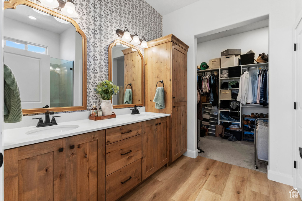 Full bathroom featuring wallpapered walls, wood finished floors, double vanity, a stall shower, and a walk in closet
