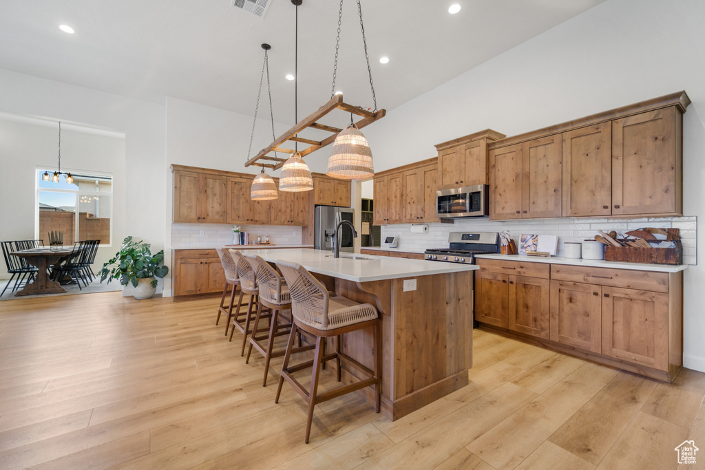 Kitchen featuring stainless steel appliances, a kitchen island with sink, a towering ceiling, a breakfast bar, and backsplash