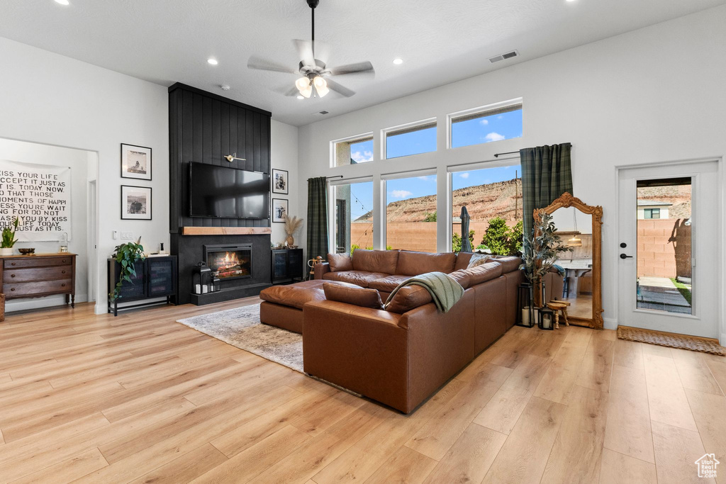 Living room with a fireplace, ceiling fan, light wood-style flooring, a towering ceiling, and recessed lighting