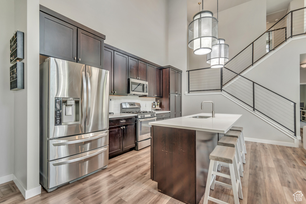 Kitchen with stainless steel appliances, light wood-style floors, light countertops, and a high ceiling