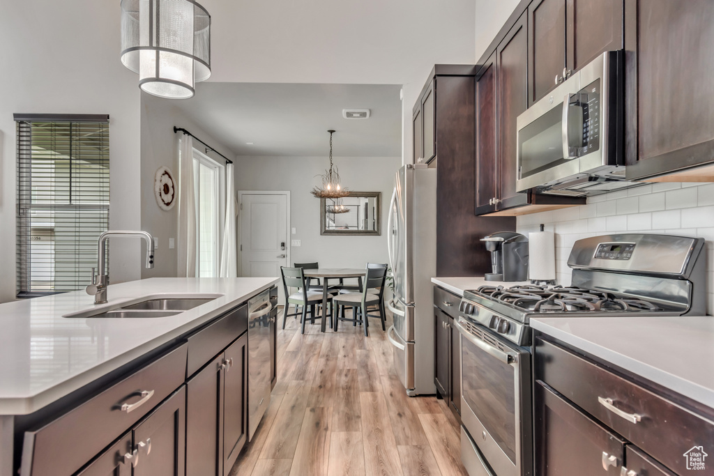Kitchen with appliances with stainless steel finishes, light countertops, dark brown cabinetry, light wood-style floors, and decorative backsplash