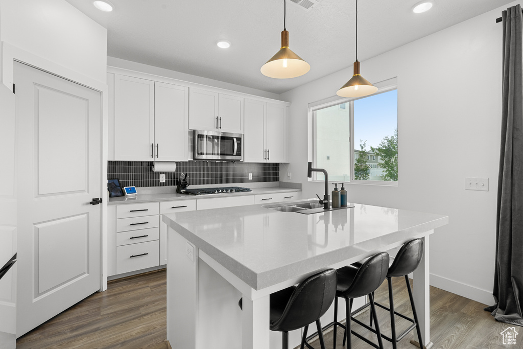 Kitchen featuring stainless steel microwave, cooktop, wood finished floors, tasteful backsplash, and recessed lighting