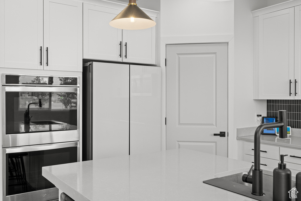 Kitchen with stainless steel double oven, white fridge, white cabinetry, and decorative backsplash