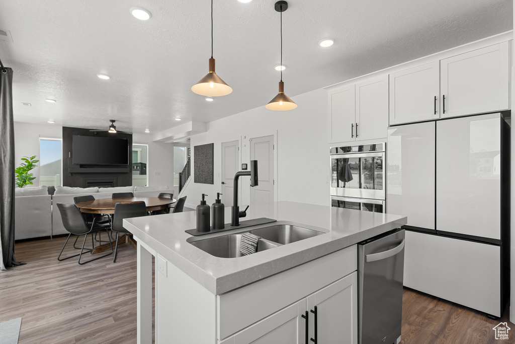 Kitchen with stainless steel appliances, light wood-type flooring, white cabinets, hanging light fixtures, and open floor plan