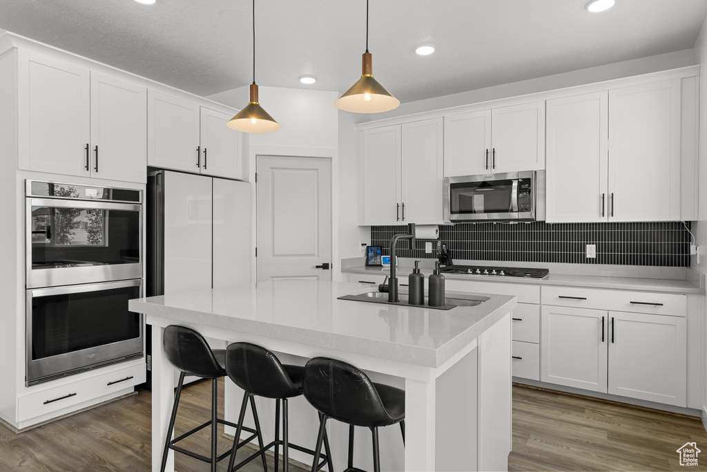 Kitchen featuring stainless steel appliances, white cabinets, a kitchen bar, decorative backsplash, and pendant lighting