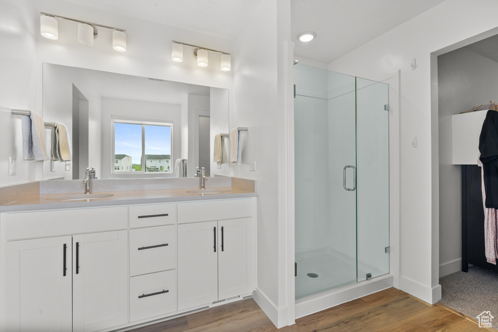 Bathroom with a shower stall, double vanity, and wood finished floors