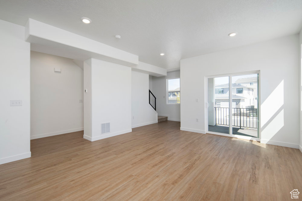 Unfurnished living room with light wood-type flooring, stairs, and recessed lighting