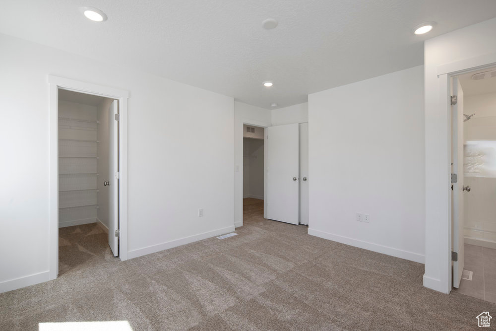 Unfurnished bedroom featuring a walk in closet, carpet floors, recessed lighting, a closet, and ensuite bath