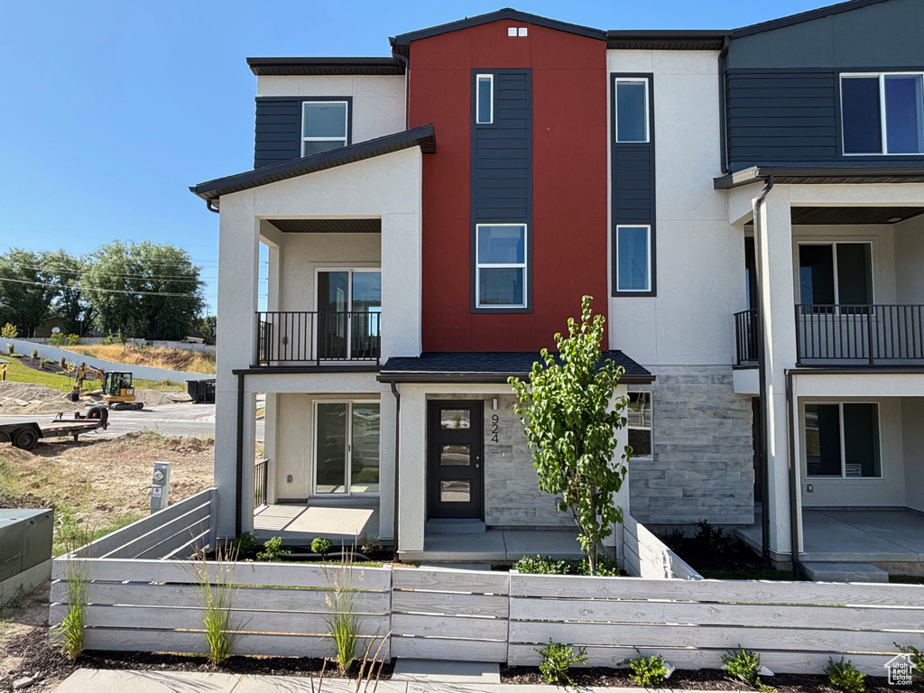 View of front facade with a balcony, a fenced front yard, stucco siding, and stone siding