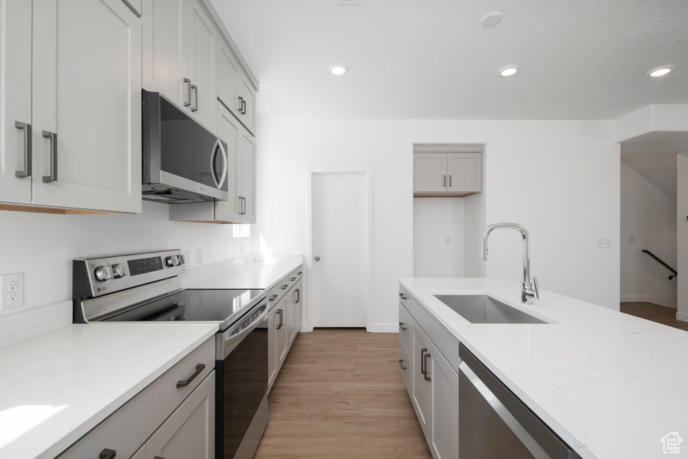 Kitchen with stainless steel appliances, light wood-style flooring, recessed lighting, and light stone countertops