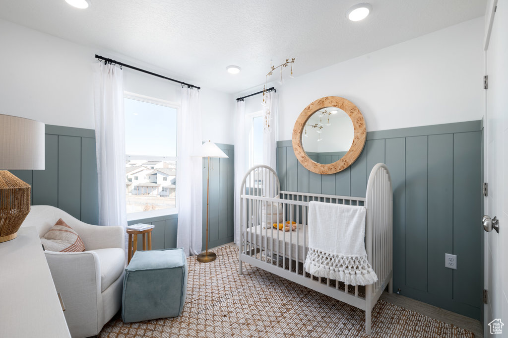 Bedroom featuring a wainscoted wall, a crib, and a decorative wall
