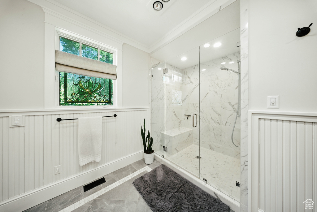Full bath with crown molding, a marble finish shower, and a wainscoted wall