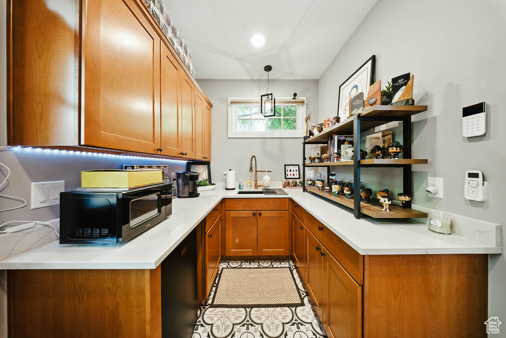 Kitchen with black microwave, brown cabinetry, light countertops, pendant lighting, and open shelves