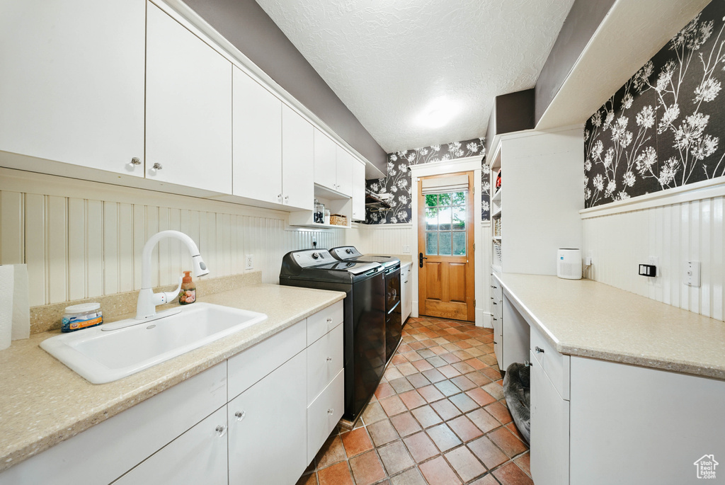 Laundry area with separate washer and dryer, a wainscoted wall, wallpapered walls, cabinet space, and a textured ceiling
