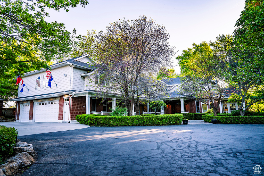 View of front of house featuring brick siding, a garage, covered porch, and asphalt driveway