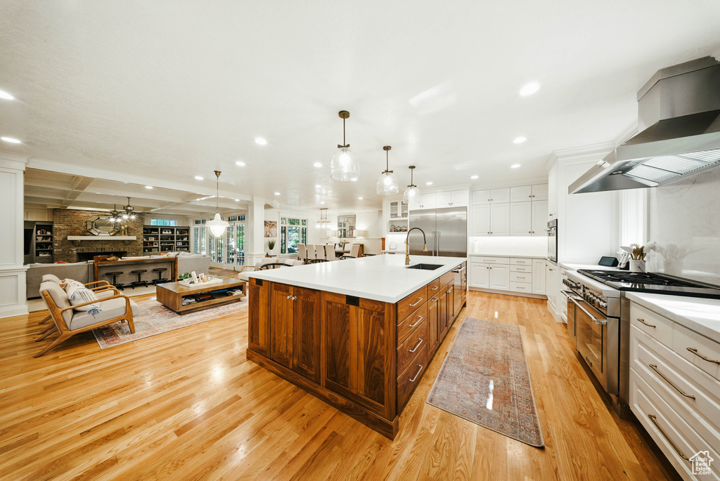 Kitchen featuring premium appliances, wall chimney exhaust hood, light wood-style flooring, white cabinetry, and open floor plan