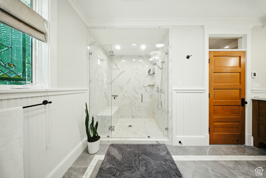 Bathroom with ornamental molding, a marble finish shower, a decorative wall, marble finish floors, and wainscoting