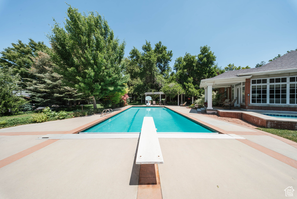 Swimming pool with a patio area, a diving board, and an in-ground hot tub