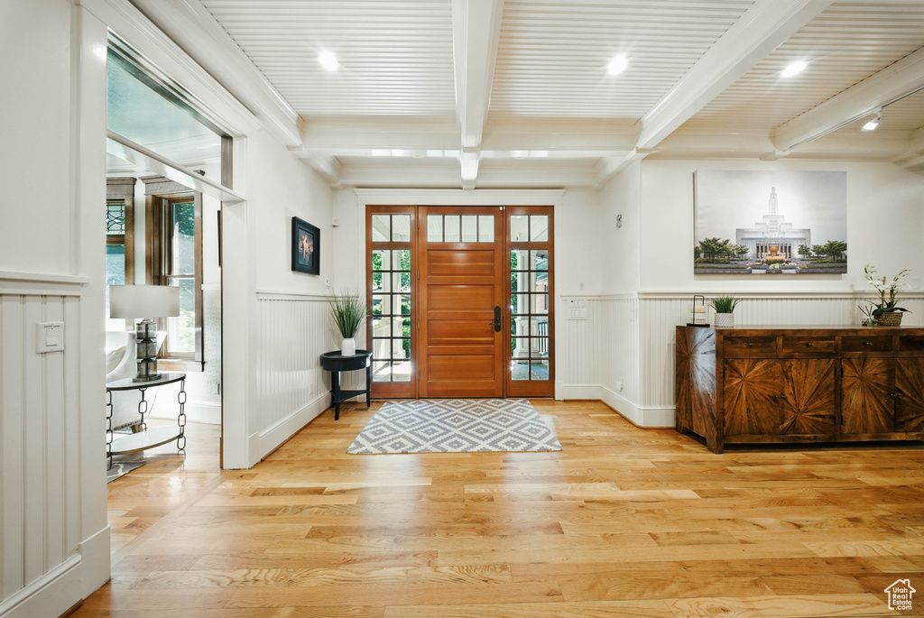 Foyer with beam ceiling, light wood finished floors, a wainscoted wall, and a decorative wall