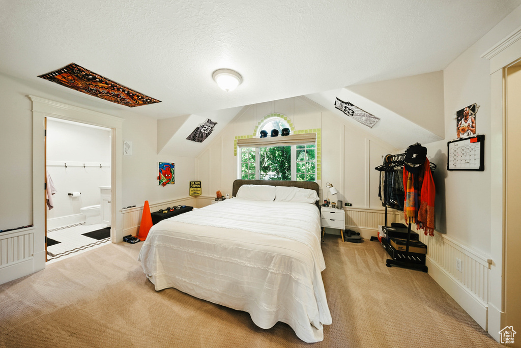Bedroom featuring light carpet, vaulted ceiling, and ensuite bathroom
