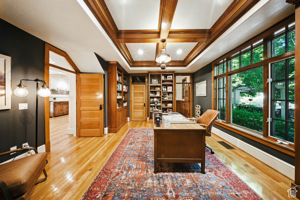 Home office with light wood finished floors, built in features, coffered ceiling, and ornamental molding