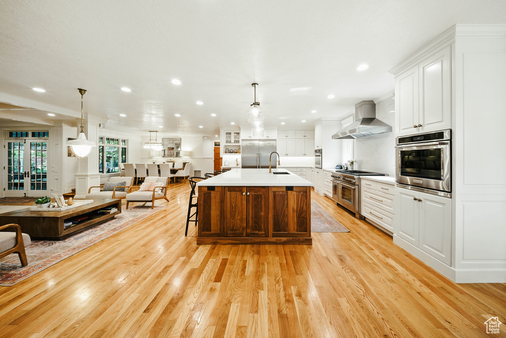 Kitchen featuring wall chimney range hood, high end appliances, open floor plan, light countertops, and light wood finished floors