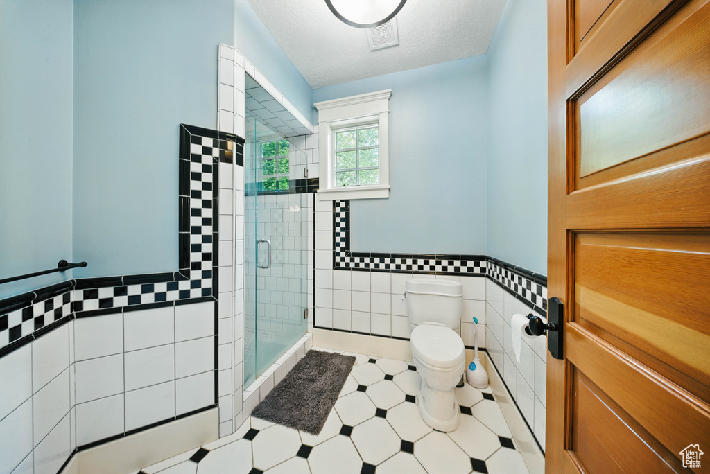 Full bathroom with tile walls, a shower stall, tile patterned floors, and a wainscoted wall