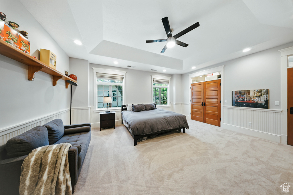 Bedroom featuring a tray ceiling, recessed lighting, light colored carpet, a wainscoted wall, and a ceiling fan