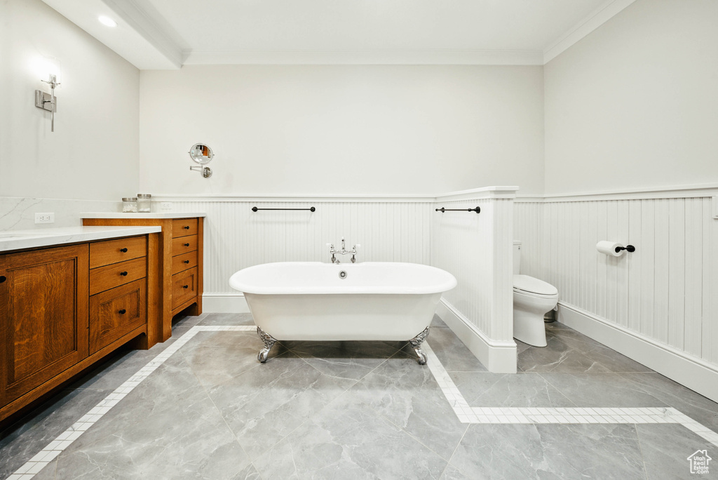 Full bathroom with marble look tiles, vanity, a freestanding bath, ornamental molding, and a wainscoted wall