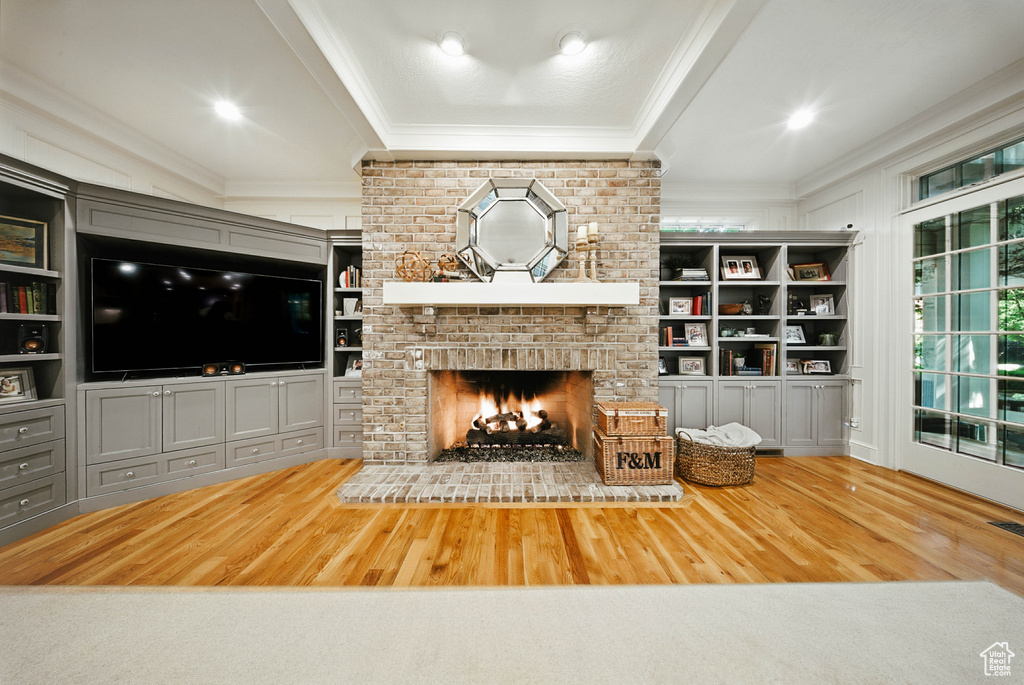 Living room with ornamental molding, wood finished floors, a brick fireplace, and built in features