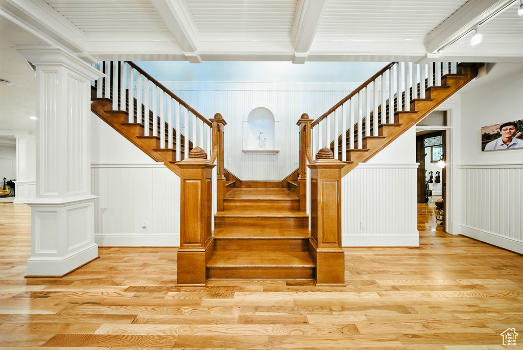 Stairway featuring decorative columns, wood finished floors, beam ceiling, a decorative wall, and a wainscoted wall