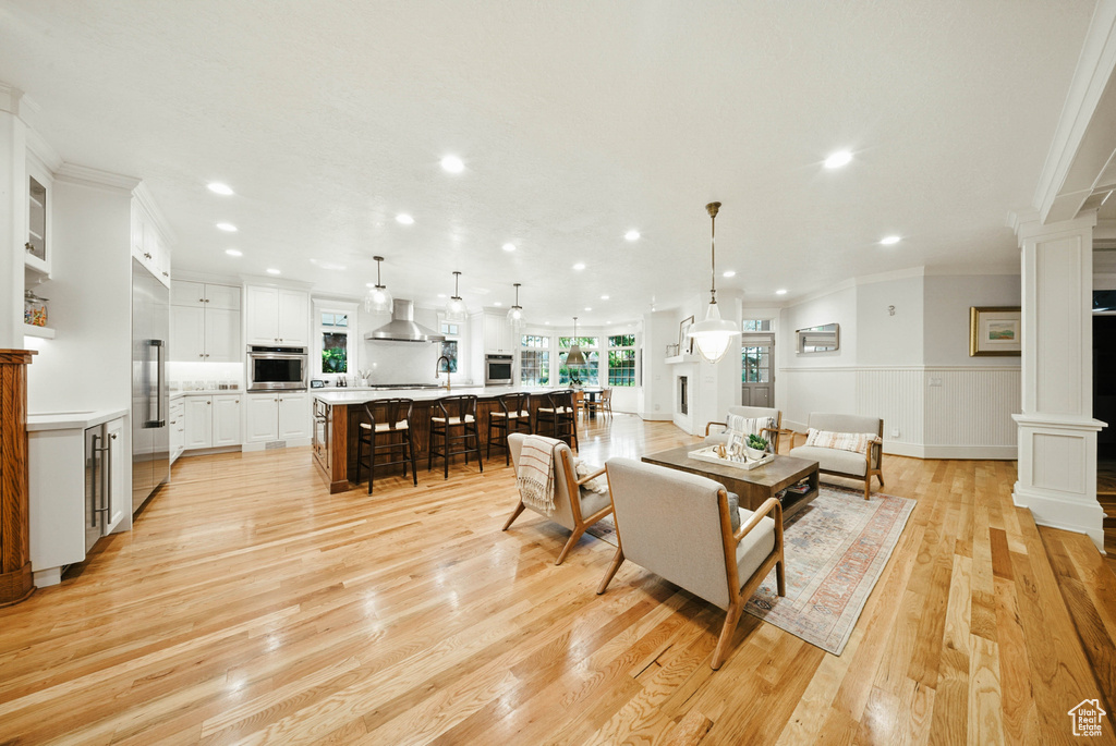 Living area with ornate columns, ornamental molding, recessed lighting, light wood-style flooring, and wainscoting