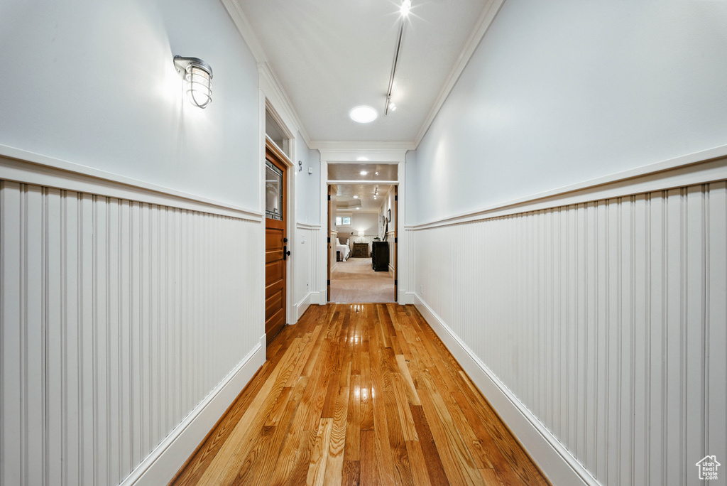 Corridor featuring a wainscoted wall, crown molding, and light wood-style floors