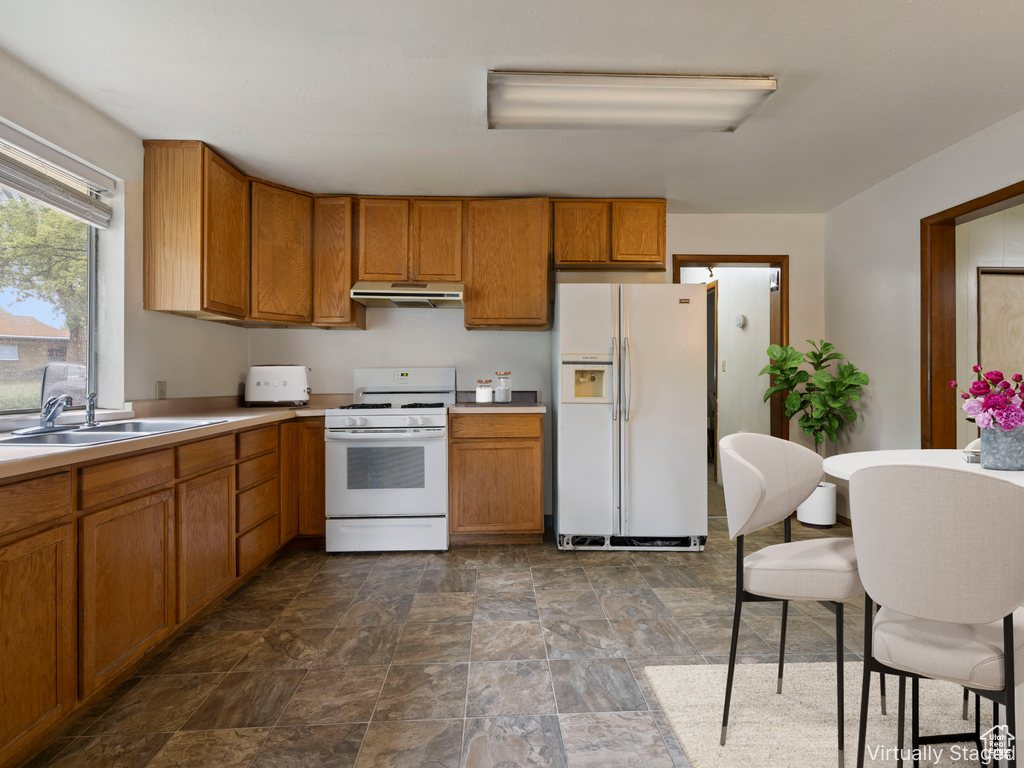 Kitchen featuring white appliances, under cabinet range hood, brown cabinetry, stone finish flooring, and light countertops