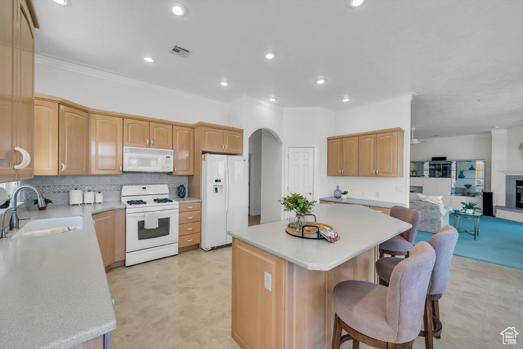 Kitchen featuring white appliances, a center island, a breakfast bar area, crown molding, and light countertops