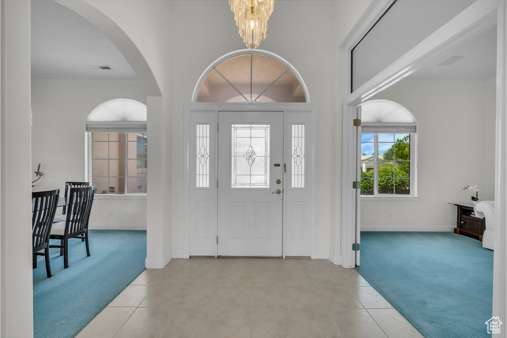 Foyer with light colored carpet, a chandelier, arched walkways, light tile patterned floors, and crown molding