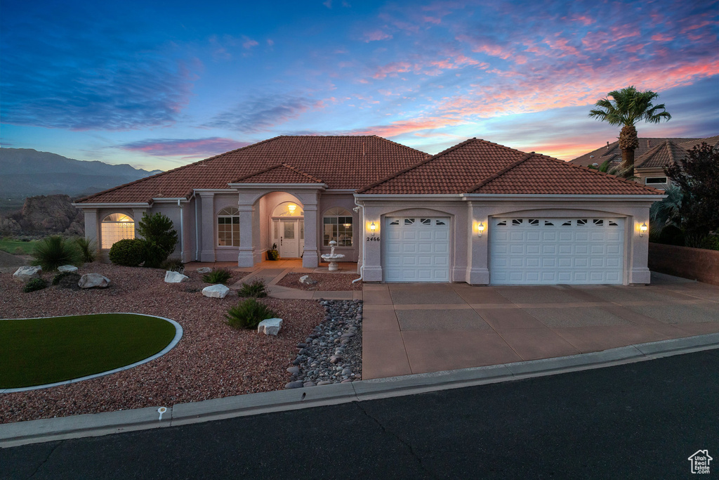 Mediterranean / spanish home featuring a garage, driveway, a tile roof, and stucco siding