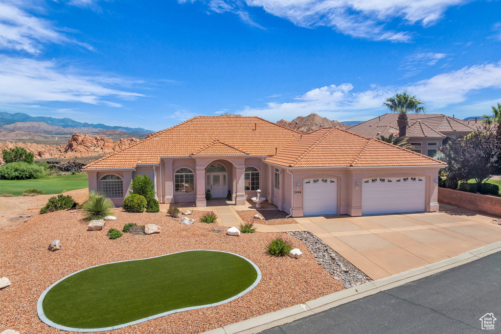 Mediterranean / spanish home with an attached garage, driveway, a tiled roof, stucco siding, and a mountain view