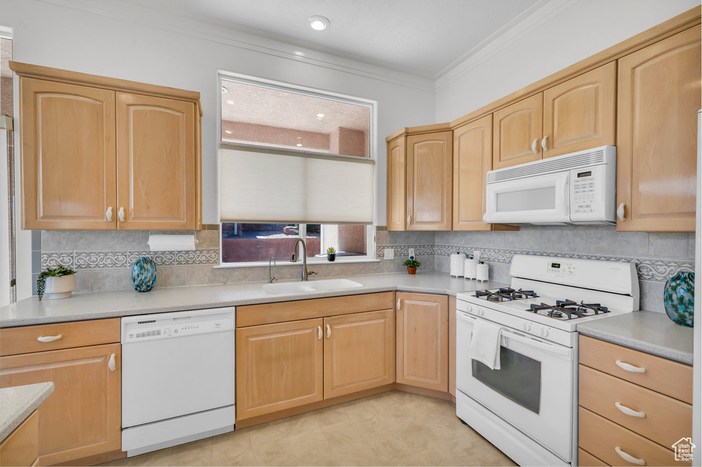 Kitchen with white appliances, ornamental molding, light brown cabinets, tasteful backsplash, and light countertops