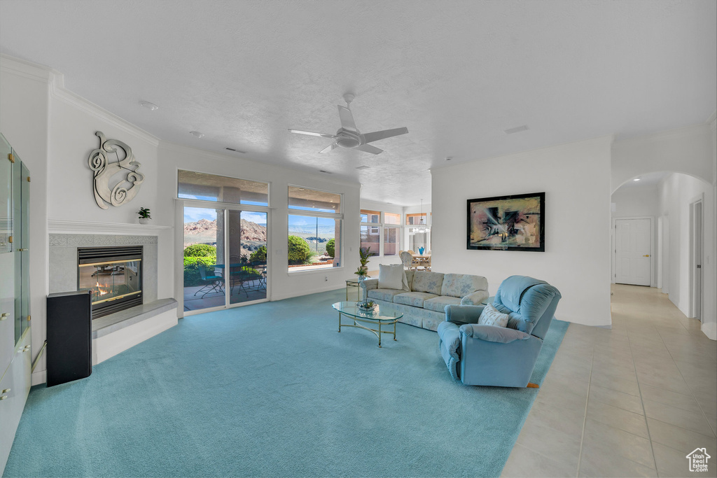 Tiled living room featuring arched walkways, a ceiling fan, a fireplace, and crown molding