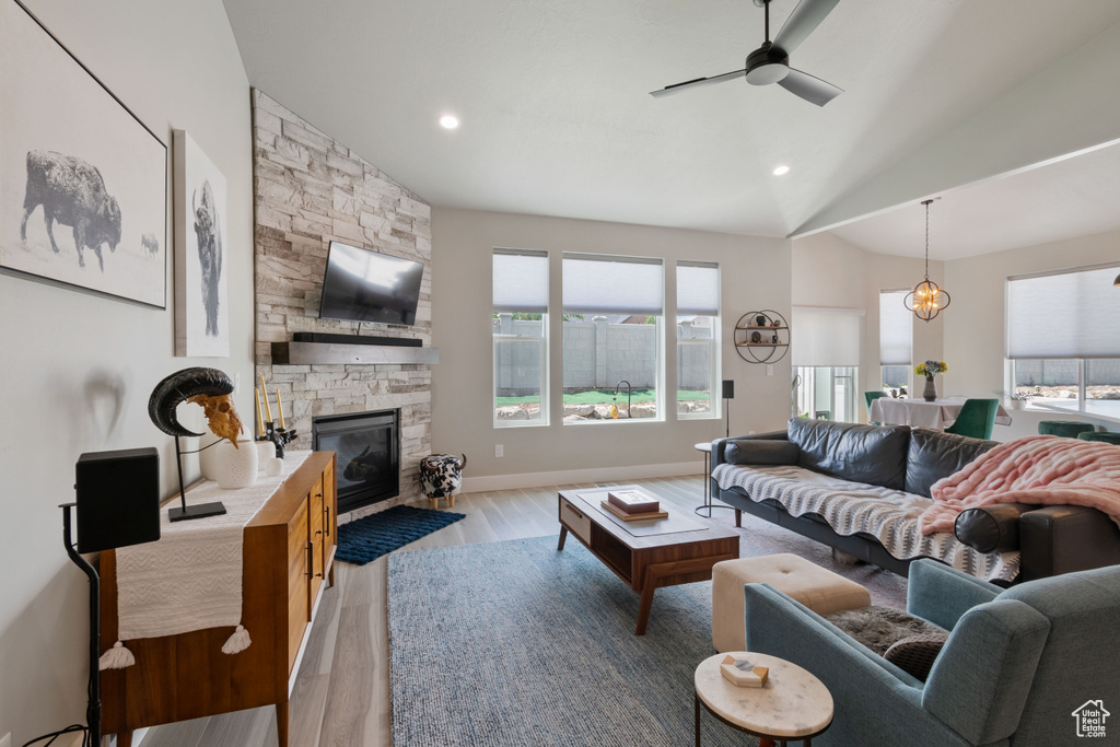 Living area featuring light wood-type flooring, a ceiling fan, a stone fireplace, vaulted ceiling, and recessed lighting