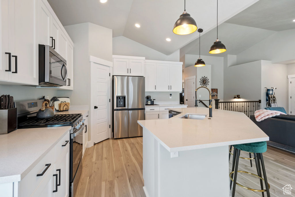 Kitchen featuring appliances with stainless steel finishes, vaulted ceiling, light wood-type flooring, a breakfast bar, and open floor plan