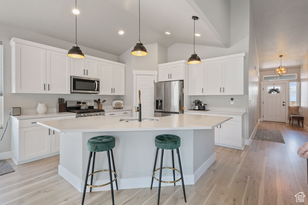Kitchen with stainless steel appliances, a center island with sink, light countertops, light wood-style flooring, and a breakfast bar area