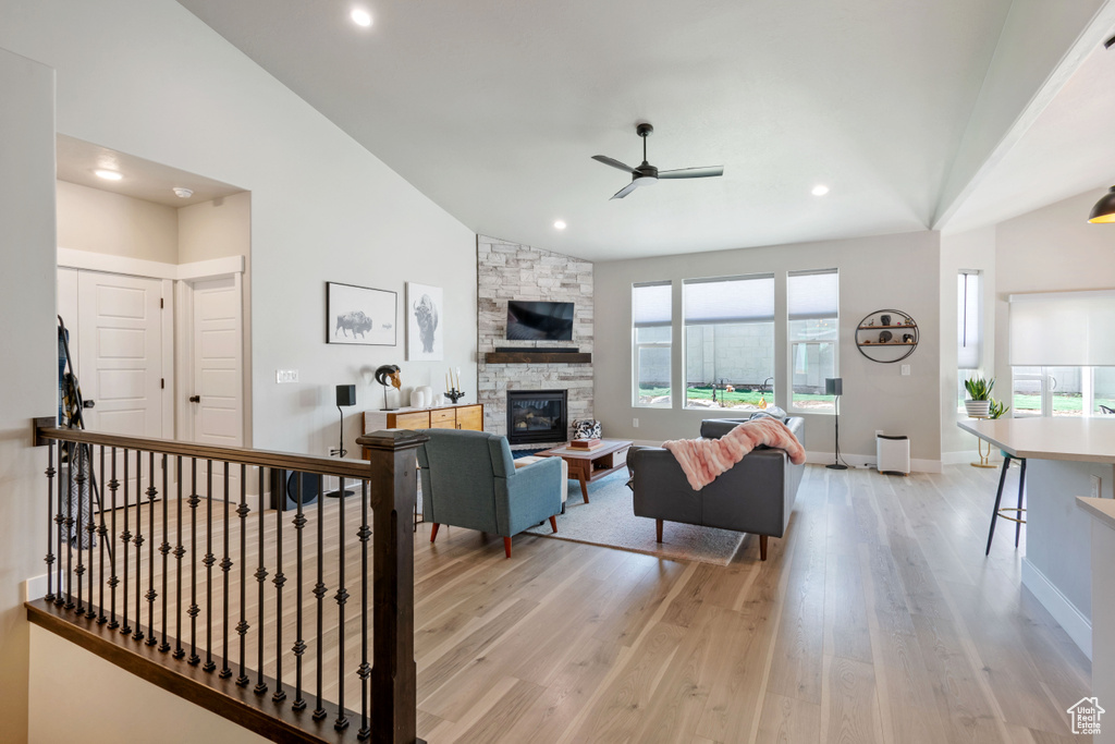 Living area featuring a ceiling fan, lofted ceiling, light wood-type flooring, a stone fireplace, and recessed lighting