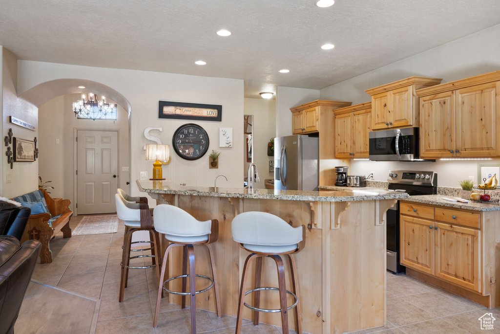 Kitchen featuring stainless steel appliances, a kitchen bar, light stone counters, arched walkways, and recessed lighting