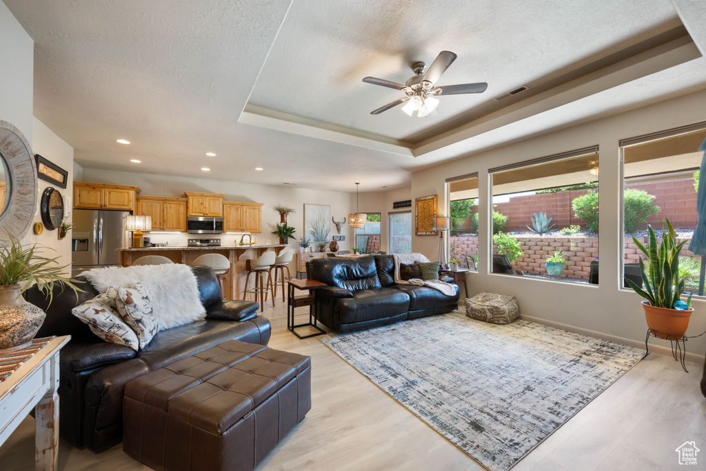 Living area featuring a ceiling fan, a tray ceiling, light wood-style floors, and recessed lighting