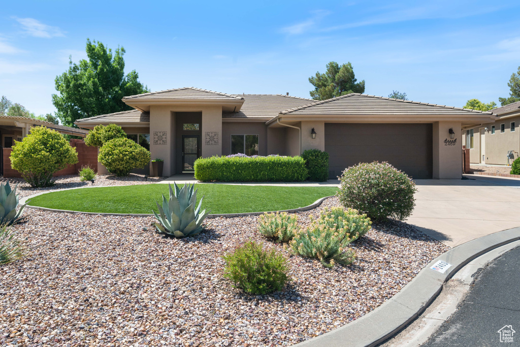 Prairie-style home with a tiled roof, an attached garage, concrete driveway, stucco siding, and a front yard