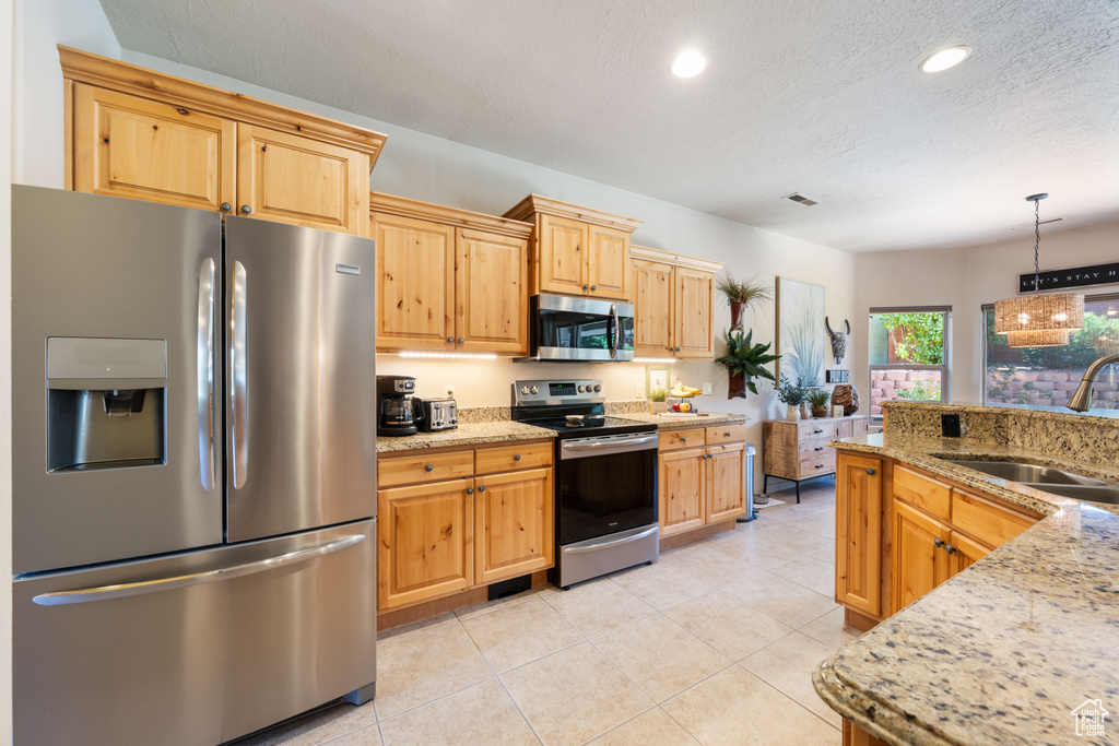 Kitchen featuring appliances with stainless steel finishes, recessed lighting, light stone counters, pendant lighting, and light tile patterned floors