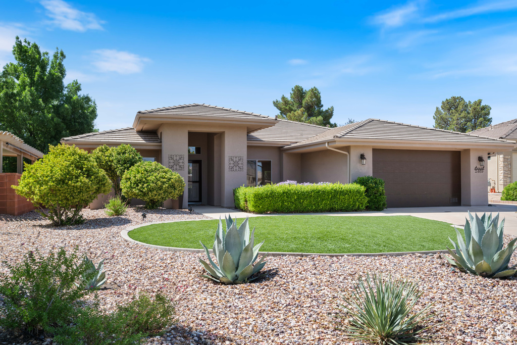 Prairie-style house featuring a front lawn, stucco siding, a tile roof, a garage, and driveway